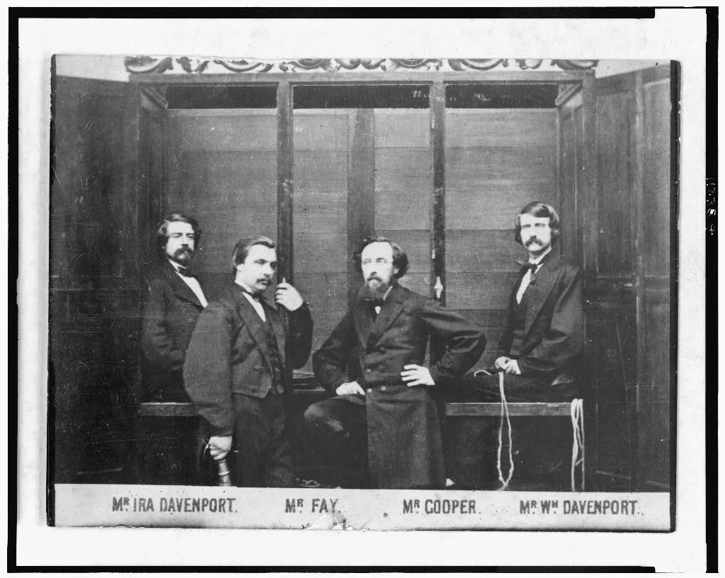Les frères Davenport sont assis et attachés dans leur cabinet de spectacle ouvert, avec des instruments de musique disposés au-dessus d’eux et entre eux.